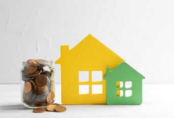 Wall Mural - House figures and jar of coins on table against light background