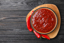 Bowl Of Hot Chili Sauce With Red Peppers On Dark Wooden Background, Top View. Space For Text