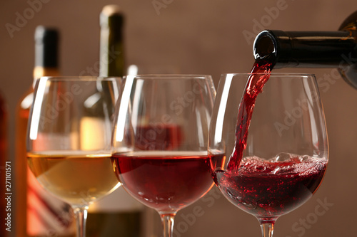 Fotomural Pouring wine from bottle into glass on blurred background, closeup