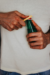 Man in a light color t-shirt opens a green bottle of fizzy drink with a yellow opener