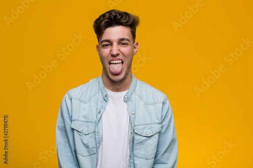 Cuadros en Lienzo Young handsome student wearing a denim shirt funny and friendly sticking out him tongue