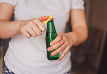 Woman In A Light Color T-shirt Opens A Green Bottle Of Fizzy Drink With A Yellow Opener