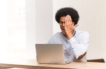 Wall Mural - Young black man using his laptop shouting happy and covering face with hand