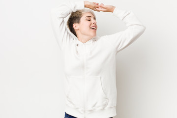 Young curvy woman wearing a white hoodie stretching arms, relaxed position.