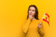© Asier - Young european woman holding a spanish flag looking sideways with doubtful and skeptical expression.