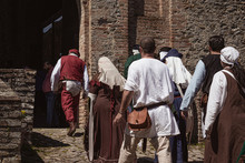 Group Of Unrecognizable People Dressed In Medieval Costumes Walking Down An Ancient Street Leading To A Castle