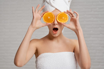 Model in towels holding two pieces of orange, closing eyes.