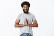 © Cookie Studio - Namaste friends. Friendly-looking happy and peaceful african american mature bearded guy with curly hair and tattoos in glasses smiling at camera greeting with asian style bow, holding palms together