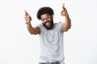 © Cookie Studio - You rock man. Portrait of joyful good-looking emotive dark-skinned guy with afro hairstyle and beard pointing finger pistols at camera with raised hands and broad smile as liking dance moves of friend