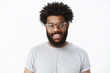 © Cookie Studio - Close-up shot of charming pleasant and delighted dark-skinned bearded male customer in glasses with afro hairstyle in grey casual t-shirt smiling joyfully as having great mood over gray background
