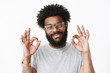 © Cookie Studio - Close-up shot of kind and friendly adult african american bearded guy with pierced nose and afro hairstyle smiling delighted and sincere showing okay gesture, feeling fine confirming work done