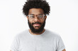 © Cookie Studio - Friendly-looking outgoing and nice african american bearded male digital nomad in glasses with afro hairstyle smiling with delighted and assertive expression posing over gray background