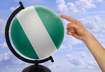 Wall Mural - The index finger of a male hand points to a globe with a colored national state flag nigeria