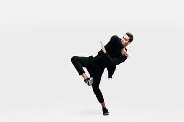 Wall Mural - Stylish young man wearing a black sweatshirt and black pants makes stylized movements of  hip-poh