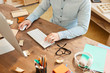 © Seventyfour - Close-up of unrecognizable creative web designer in casual shirt sitting at wooden table with messy crumpled papers and using desktop computer