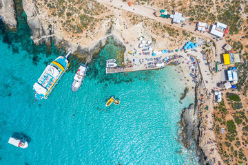 Aerial view famous Blue Lagoon in the Mediterranean Sea. Comino Island, Malta. Beach and vacationers, a bay pier with ships and boats.