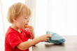Side view of blonde child in red t-shirt with pleasure eating corn sticks holding and looking in pack on table at home