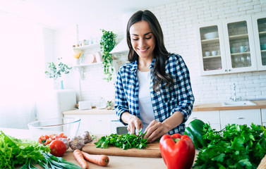 Wall Mural - Beautiful young woman is preparing vegetable salad in the kitchen. Healthy Food. Vegan Salad. Diet. Dieting Concept. Healthy Lifestyle. Cooking At Home. Prepare Food. Cutting ingredients on table