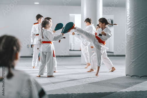 Leinwand Poster Group of sporty Caucasian children in doboks having taekwondo class in white gym