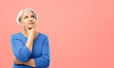 old people and decision making concept - portrait of senior woman in blue sweater thinking over pink or living coral background