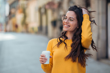 Portrait of a happy young woman in the city holding takeout drink.