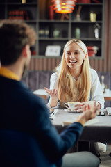 Smiling Caucasian blonde businesswoman dressed smart casual discussing with her male colleague about project while sitting in coffe shop.