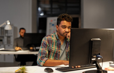 deadline, technology and people concept - sad creative man with computer working at night office