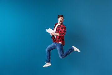 Jumping young man with book on color background