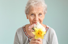 Portrait Of Senior Woman With Bouquet Of Flowers On Grey Background