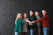 © Pixel-Shot - Group of young business people putting hands together on dark brick background