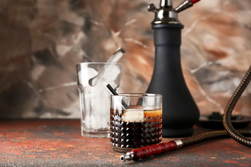 Glass of cold whiskey with hookah on table