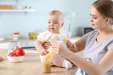 Mother feeding her little baby in kitchen at home