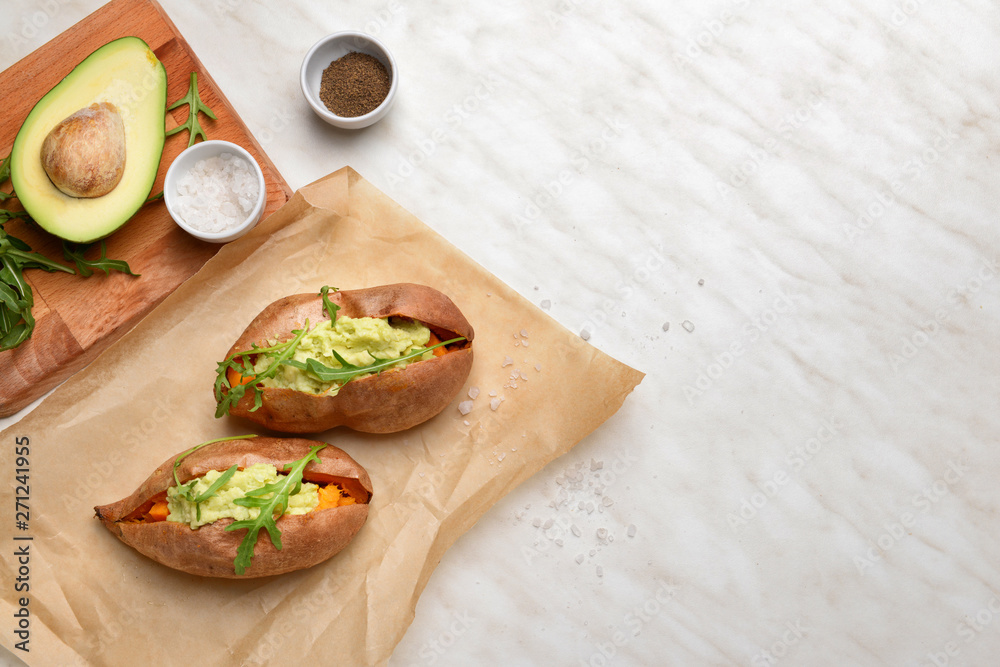Baked sweet potato with guacamole and arugula on light table