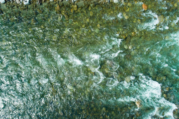 Top view of mountain river water with rocks and splashes. Background of fresh water with fast rapids in alpine river.