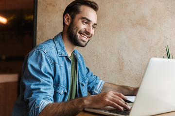 Photo of happy smiling man looking at laptop while working in cafe indoors