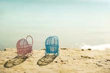 The Concept Of Pregnancy At Sea. Pink And Blue Miniature Strollers On The Beach At Sunset