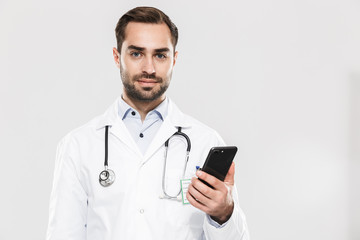 Portrait of attractive young medical doctor with stethoscope working in clinic and holding cellphone