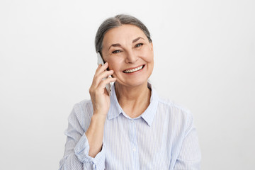 Wall Mural - Attractive good looking mature European female on retirement spending hours on talking on smart phone to old friend using unlimited mobile package. Charming middle aged lady enjoying phone talk