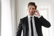 © Drobot Dean - Photo of smiling handsome businessman talking on cellphone in hotel apartment