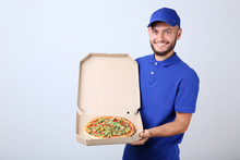 Delivery Man With Pizza In Cardboard Box On Grey Background