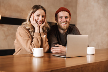 Sticker - Happy young loving couple in cafe using laptop computer drinking coffee.