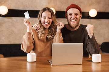 Sticker - Excited young loving couple in cafe using laptop computer drinking coffee holding credit card.