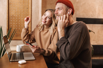 Sticker - Young loving couple in cafe using laptop computer drinking coffee listening music with earphones.