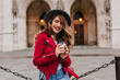 © Look! - Beautiful caucasian woman smiling to camera while drinking latte beside museum. Adorable chilling girl with wavy hair posing near historical place during travel.