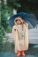 Portrait of cute little girl wearing raincoat and holding umbrella on the raining,Thailand people