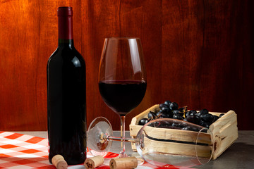 Bottle of red wine in wine cellar for tasting. Red wooden background with wooden box with grapes. Wine tradition and culture concept.