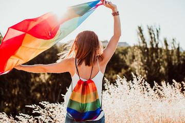 .Uoung and pretty woman proudly wearing the gay flag outdoors at sunset. Fighting for the rights and freedoms of human beings. Universal love. Lifestyle