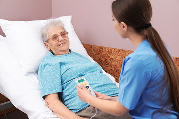 Canvas Print - Nurse assisting senior woman lying on bed in hospital ward