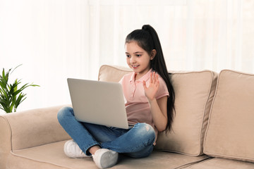 Wall Mural - Little girl using video chat on laptop at home