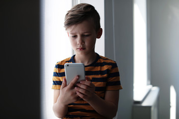 sad little child with smartphone indoors. danger of internet